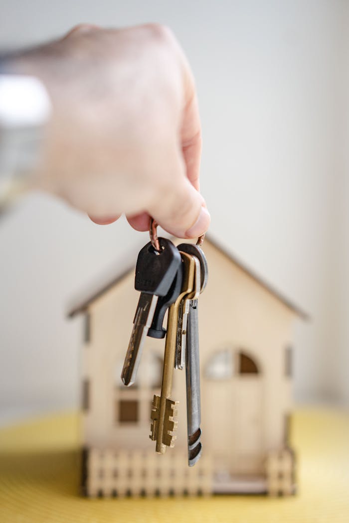 Home Close-up of a hand holding keys with a miniature wooden house in the background, symbolizing real estate investment.